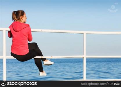 Woman sitting on pier looking at horizon outdoors. Woman resting after doing sports outdoors. Fitness girl in sportswear sitting on pier relaxing looking at horizon back view