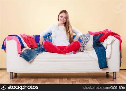 Woman sitting on sofa couch in messy living room. Young girl surrounded by many stack of clothes. Disorder and mess at home.. Woman sitting on sofa in messy room at home.