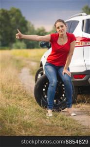 Woman sitting on spare tire at broken car and hitchhiking