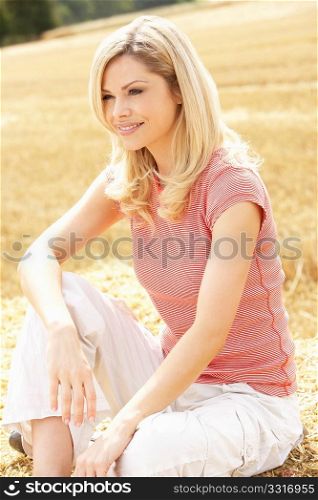 Woman Sitting On Straw Bales In Harvested Field