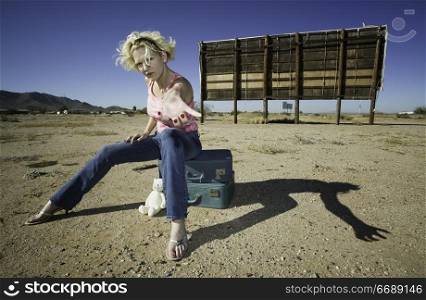 Woman sitting on suitcases in front of an old billboard reaching to the camera