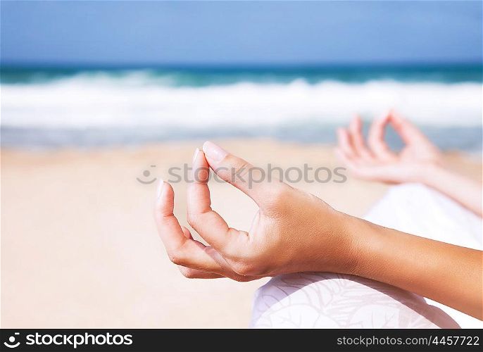 Woman sitting on the beach in lotus pose and meditating, body part, doing yoga exercise outdoors, zen balance and relaxation concept