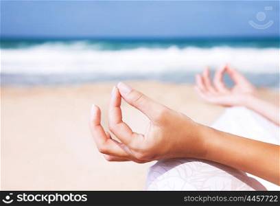Woman sitting on the beach in lotus pose and meditating, body part, doing yoga exercise outdoors, zen balance and relaxation concept