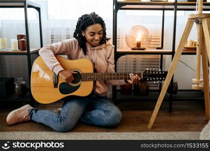 Woman sitting on the floor and play the guitar at home, closeup view. Pretty lady with musical instrument relax in the room, female music lover resting. Woman sitting on the floor and play the guitar