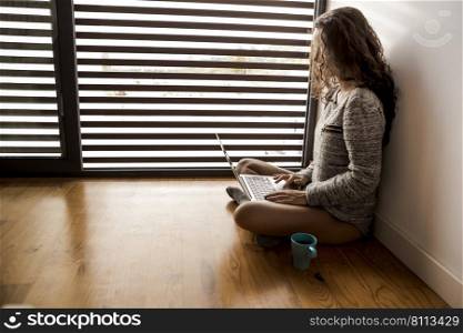 Woman sitting on the floor drinking a coffee and working on a laptop