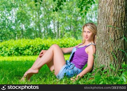 woman sitting on the green grass in the park near the tree