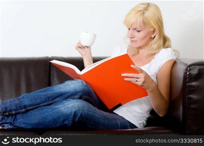 Woman sitting on the sofa reading and drinking coffee