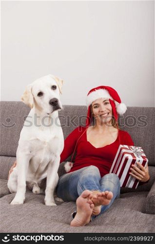 Woman sitting on the sofa with her dog and wearing a santa hat  