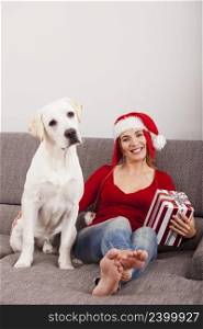 Woman sitting on the sofa with her dog and wearing a santa hat  