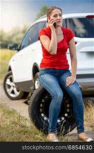 Woman sitting on the spare tire at roadside and calling for help