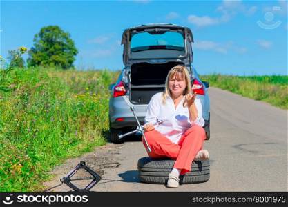 woman sitting on the spare wheel with the tools on the road