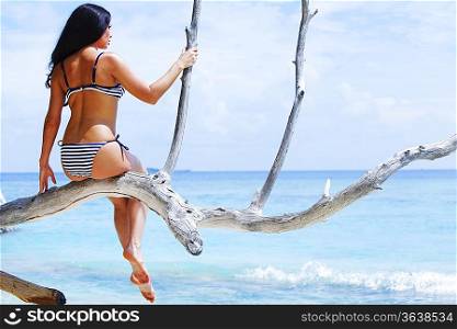 Woman sitting on tree near sea