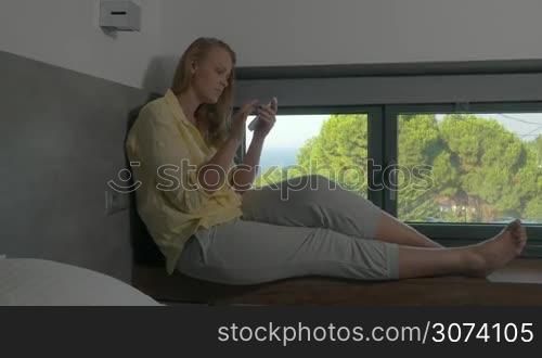 Woman sitting on windowsill and typing on phone