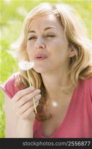 Woman sitting outdoors blowing dandelion head