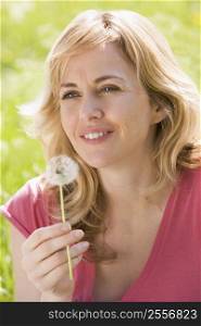 Woman sitting outdoors holding dandelion head smiling
