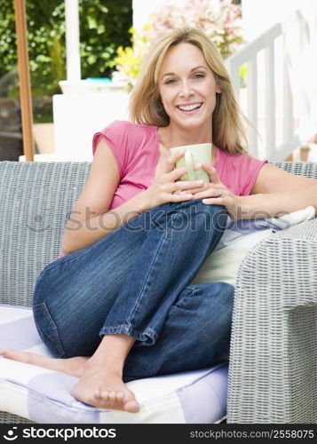 Woman sitting outdoors on patio with coffee smiling