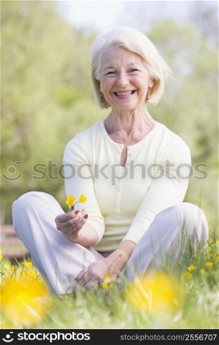 Woman sitting outdoors smiling and holding a Buttercup flower