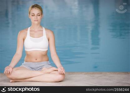 Woman sitting poolside doing yoga