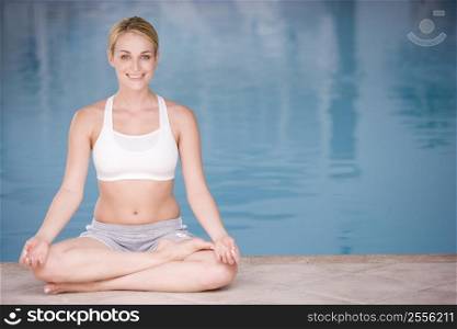 Woman sitting poolside doing yoga smiling
