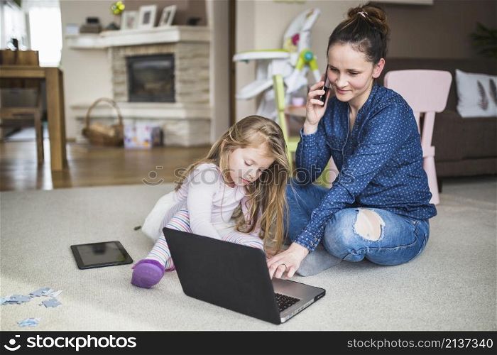 woman sitting with her daughter talking cellphone while using laptop