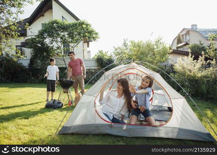 woman sitting with her daughter tent during her husband son cooking barbecue grill