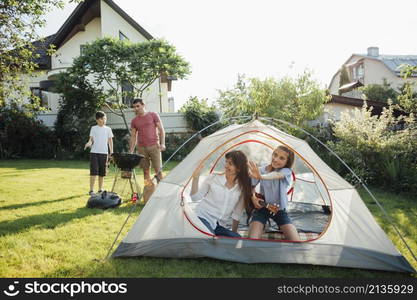 woman sitting with her daughter tent during her husband son cooking barbecue grill