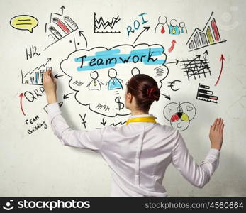 Woman sketching business strategy. Back view of businesswoman drawing colorful business ideas on wall