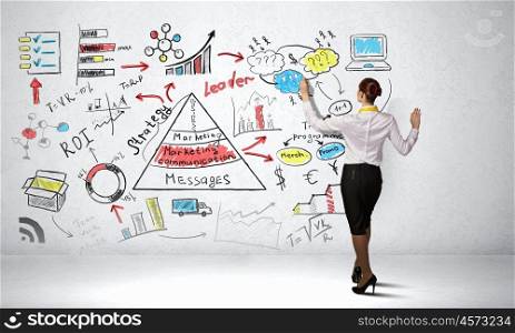 Woman sketching business strategy. Back view of businesswoman drawing colorful business ideas on wall