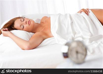 Woman sleeping in white bed, alarm clock in foreground