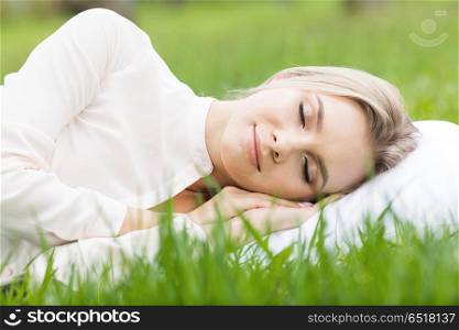 Woman sleeping on grass. Young woman sleeping on white pillow in fresh spring grass
