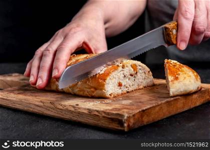 Woman Slices Homemade Wholemeal Multigrain Bread with Flax Seeds and Sesame on Wooden Board on Dark Table.. Woman Slices Homemade Wholemeal Multigrain Bread with Flax Seeds and Sesame on Wooden Board on Dark Table