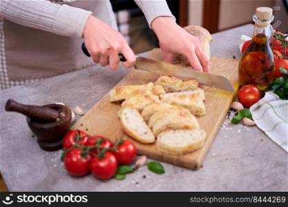 Woman slicing French bread baguette on wooden bread board.. Woman slicing French bread baguette on wooden bread board