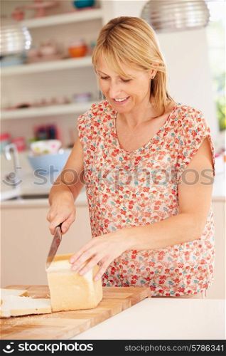 Woman Slicing Loaf Of Bread In Kitchen