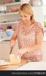 Woman Slicing Loaf Of Bread In Kitchen