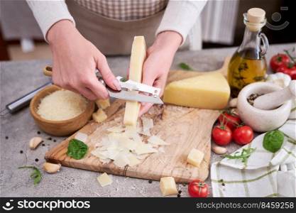 Woman slicing Parmesan cheese on a wooden cutting board at domestic kitchen.. Woman slicing Parmesan cheese on a wooden cutting board at domestic kitchen