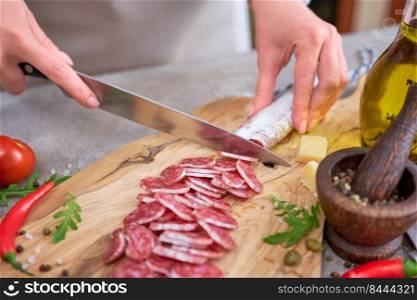 Woman slicing Spanish sausage fuet salami with knife on a domestic kitchen.. Woman slicing Spanish sausage fuet salami with knife on a domestic kitchen