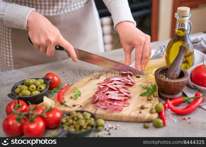 Woman slicing Spanish sausage fuet salami with knife on a domestic kitchen.. Woman slicing Spanish sausage fuet salami with knife on a domestic kitchen