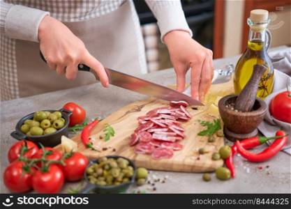 Woman slicing Spanish sausage fuet salami with knife on a domestic kitchen.. Woman slicing Spanish sausage fuet salami with knife on a domestic kitchen