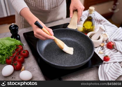 Woman smear olive oil on frying pan with silicone brush at domestic kitchen.. Woman smear olive oil on frying pan with silicone brush at domestic kitchen