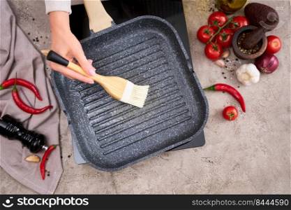 Woman smear olive oil on grill frying pan with silicone brush at domestic kitchen.. Woman smear olive oil on grill frying pan with silicone brush at domestic kitchen
