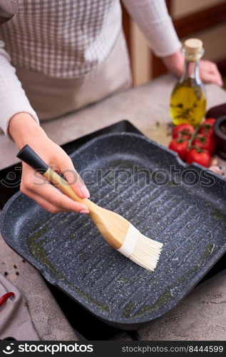 Woman smear olive oil on grill frying pan with silicone brush at domestic kitchen.. Woman smear olive oil on grill frying pan with silicone brush at domestic kitchen