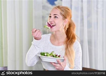 Woman smiles while taking a bite of a healthy salad indoors on an out of focus background. Healthy lifestyle concept.. Woman smiles while eating a healthy salad