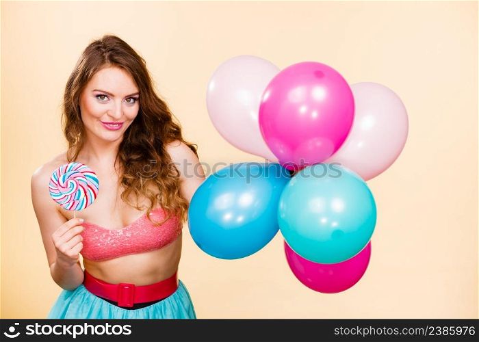 Woman smiling cheerful girl holding colorful balloons and sweet lollipop in hands. Summer holidays, celebration and happiness concept. Studio shot bright. Woman holds lollipop candy and balloons