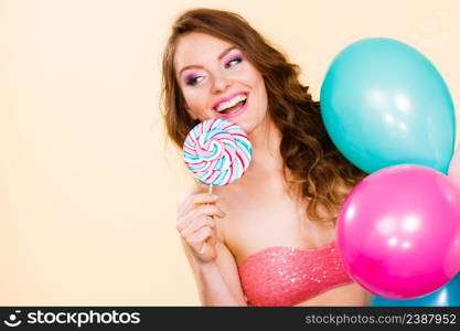 Woman smiling cheerful girl holding colorful balloons and sweet lollipop in hands. Summer holidays, celebration and happiness concept. Studio shot bright. Woman holds lollipop candy and balloons