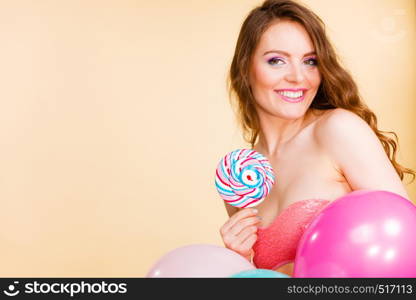 Woman smiling cheerful girl holding colorful balloons and sweet lollipop in hands. Summer holidays, celebration and happiness concept. Studio shot bright. Woman holds lollipop candy and balloons