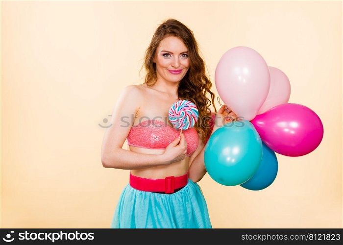 Woman smiling cheerful girl holding colorful balloons and sweet lollipop in hands. Summer holidays, celebration and happiness concept. Studio shot bright. Woman holds lollipop candy and balloons