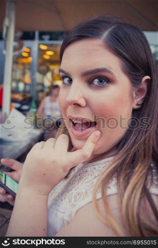 Woman smiling excited astonished happy smile at the camera while play with her phone at a cafe.