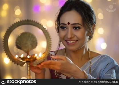 Woman smiling while lighting a lamp with diya
