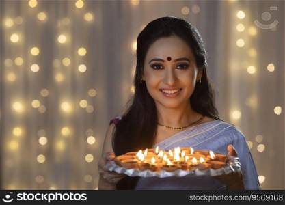 Woman smiling with a plate of diyas in her hand on the occasion of Diwali