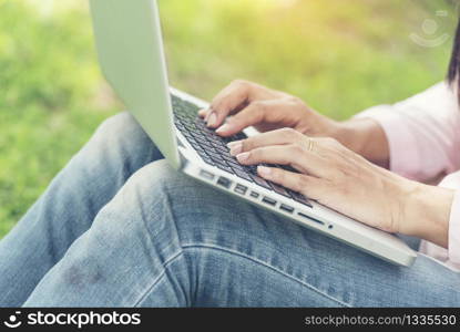 Woman Social Blogger using laptop for explore website outdoor in summertime. Enjoy outdoor lifestyle sitting on grass under big tree in the morning.